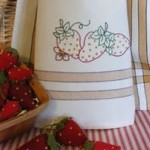 A trio of plump, ripe strawberries are embroidered on a Gold Stripe Tea Towel.